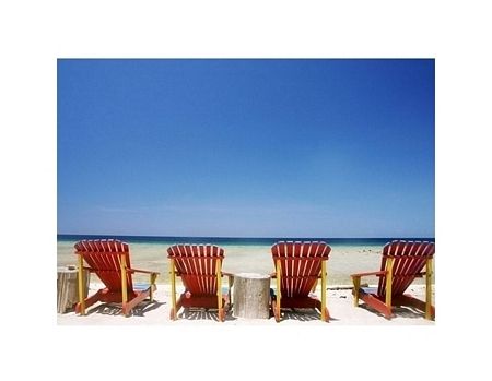 relaksujący obraz przedstawiający cztery leżaki na piaszczystej plaży z widokiem na spokojne morze i błękitne bezchmurne niebo