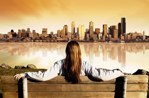 fototapeta przedstawiająca kobietę siedzącą na ławce i spoglądającą na panoramę miasta o zachodzie słońca