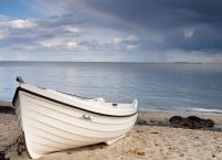 fototapeta na ścianę przedstawiająca białą łódź zacumowaną na piaszczystej plaży na tle spokojnego morza i zachmurzonego nieba