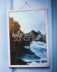 Plakat oprawiony w białą ramę przedstawiający nadmorski krajobraz oraz napis ''Hello Sunshine''