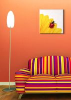 aranżacja obrazu na płótnie z biedronką i żółtym kwiatem w pokoju z pomarańczową ścianą nad pasiastą sofą