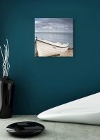 aranżacja obrazu na płótnie przedstawiającego białą łódź zacumowaną na piaszczystej plaży na tle spokojnego morza i zachmurzonego nieba w pokoju z turkusową ścianą