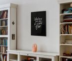 Plakat wiszący w salonie nad szafką z książkami oprawiony w czarną ramę z napisem ''Whatever you are be a good one''