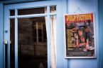 Plakat z Mią Wallace z Pulp Fiction powieszony na niebieskiej ścianie obok drzwi
