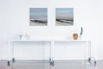Canvasy przedstawiające morskie krajobrazy powieszone na białej ścianie nad stolikiem