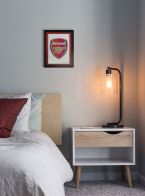 Obraz w czarnej ramie z logo angielskiego klubu Arsenal wiszący w sypialni nad łóżkiem
