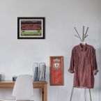 Obraz w czarnej ramce z angielskim klubem Liverpool powieszony nad biurkiem z drewna