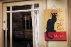 Zdjęcie przedstawiające obraz na drewnie z czarnym kotem wiszący obok drzwi