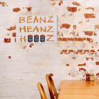 Obraz na drewnie z napisem Beanz Meanz Heinz wiszący na ścianie w restauracji