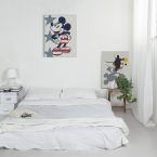 Canvas z Myszką Miki wiszący nad białym łóżkiem w minimalistycznie urządzonej sypialni