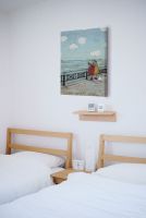 Obraz autorstwa Sam Toft powieszony w pokoju nad dwoma łóżkami z białą pościelą