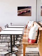 Obraz na drewnie z Ferrari wiszący na białej ścianie nad stolikami w restauracji