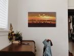Zdjęcie na którym widoczny jest obraz na płótnie ze słoniami wędrującymi o zachodzie słońca powieszony w pokoju na ścianie
