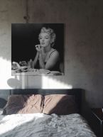 Czarno-biały obraz na płótnie przedstawiający malującą się Marylin Monroe powieszony w sypialni na szarej ścianie nad łóżkiem