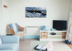 Obraz na płótnie przedstawiający morski pejzaż z latarnią morską powieszony w salonie obok telewizora
