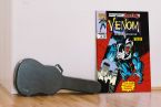 Obraz z komiksu Venom Lethal Protector Comic Cover w pokoju obok czarnego pokrowca na gitarę
