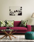 Obraz z dwiema pandami powieszony w salonie nad czerwoną kanapą z zielonymi poduszkami