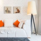 Obraz z rudym lisem powieszony na ceglanej ścianie obok obrazu z królikami nad białą kanapą z pomarańczowymi poduszkami