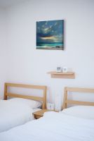 Obraz niebieskiego wybrzeża z widokiem na plaże i morze powieszony w sypialni nad łóżkami z białą pościelą