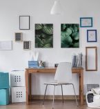 Obrazy botaniczne z liśćmi powieszone nad drewnianym biurkiem na białej ścianie