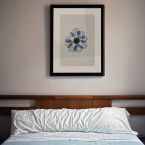 Niebieski kwiat na reprodukcji w czarnej ramie powieszonej nad łóżkiem