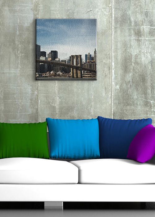aranżacja obrazu z Brooklyn Bridge i drapaczami chmur w pokoju na szarej ścianie nad białą sofą z kolorowymi poduszkami