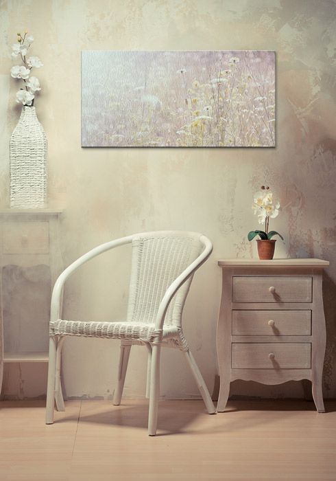 Obraz na płótnie z kwiatami powieszony nad białym ażurowym krzesłem obok małej szafki z szufladami