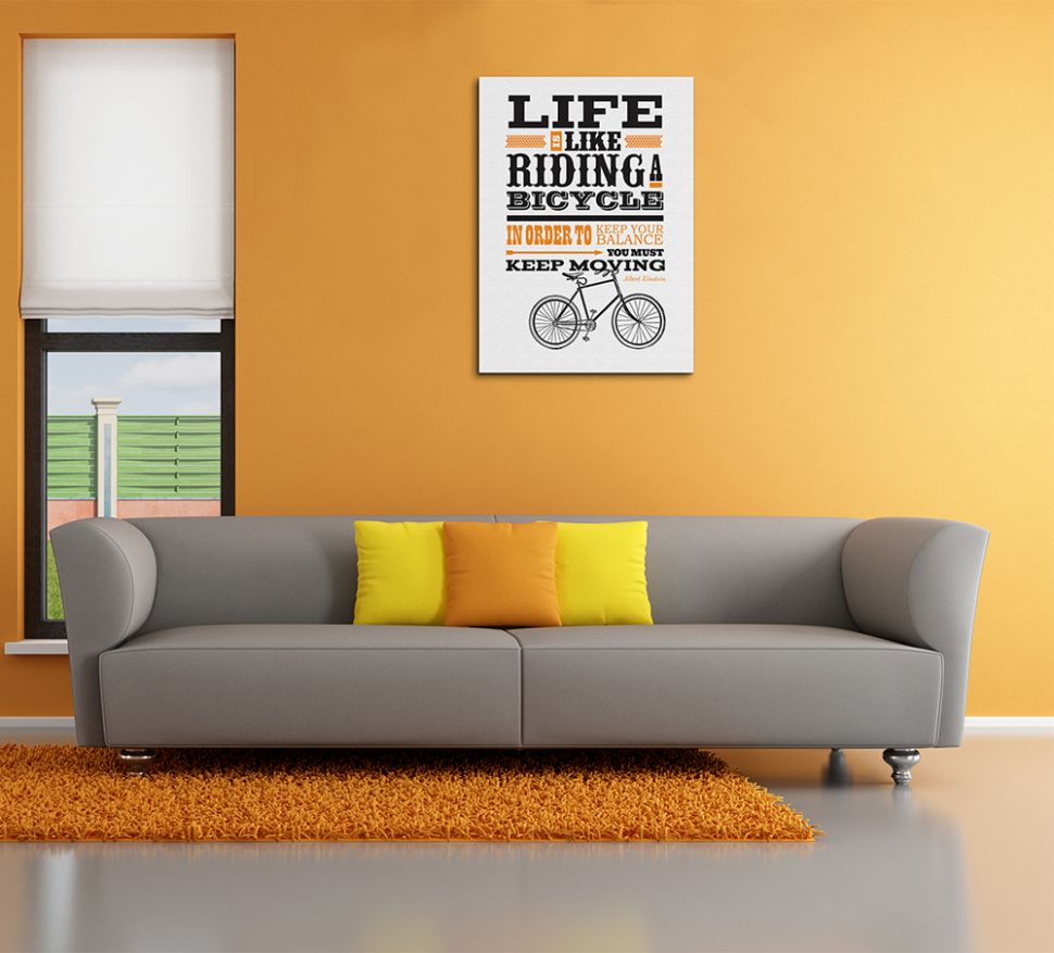 Aranżacja obrazu typograficznego z rowerem i pomarańczowym napisem w salonie nad szarą sofą