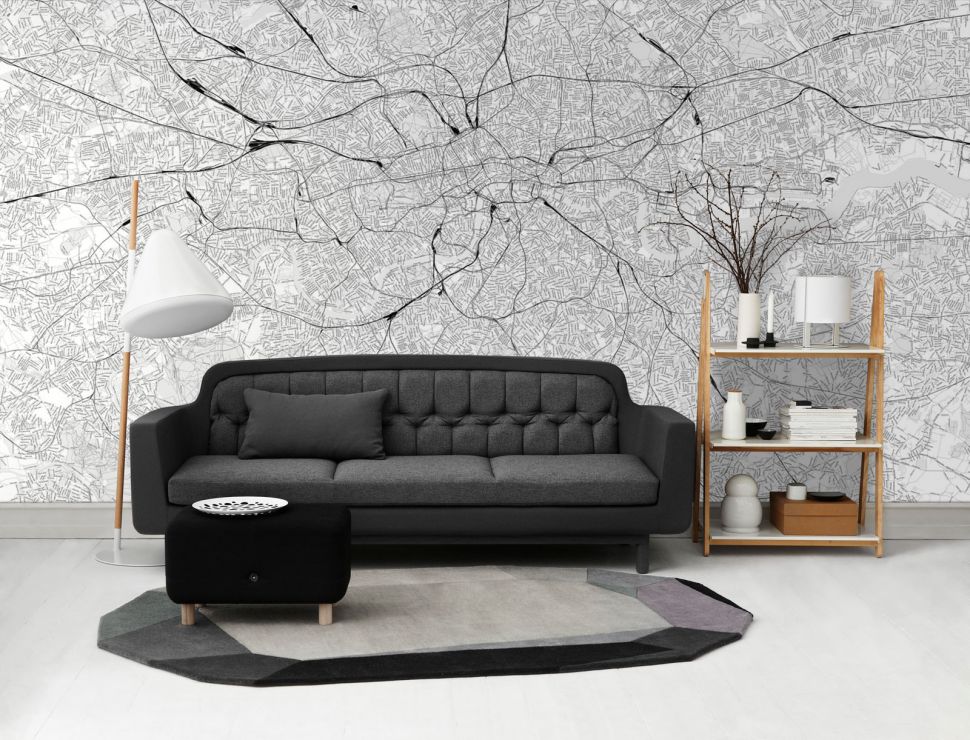 Czarno-biała, duża mapa Londynu na ścianie w salonie, umieszczona nad szarą kanapą