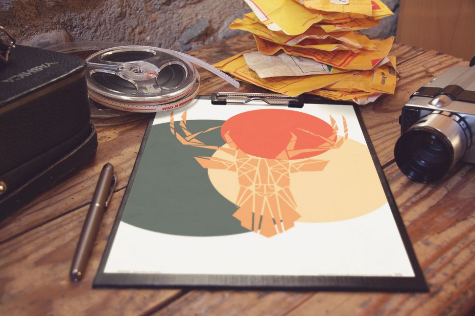 Plakat leżący na drewnianym stole przedstawiający geometrycznego, kolorowego jelenia