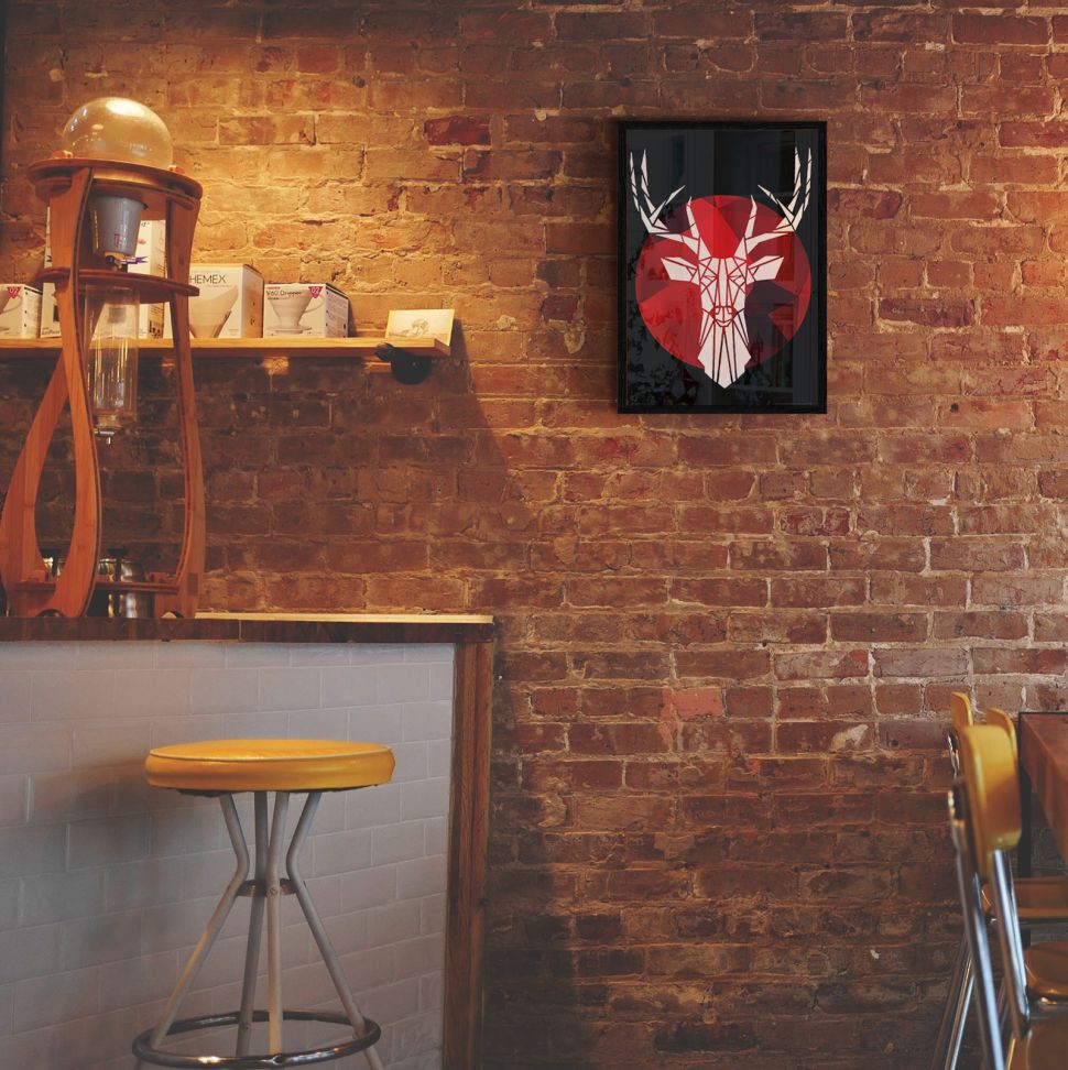 Plakat wiszący na ścianie z czerwonej cegły oprawiony w czarną ramę przedstawiający geometrycznego, białego jelenia