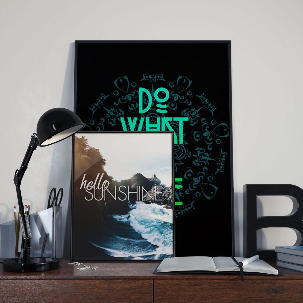Plakat stojący na biurku oprawiony w czarną ramę przedstawiający nadmorski krajobraz oraz napis ''Hello sunshine''