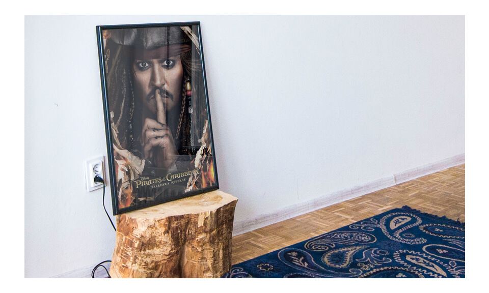 Plakat Jacka Sparrow'a oprawiony w czarną ramkę leżącą na drewnianym pniu