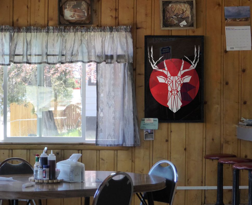 Plakat wiszący w restauracji na drewnianej ścianie oprawionego w czarną ramę przedstawiający białego, geometrycznego jelenia na kolorowym tle