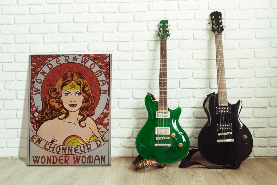 Obraz na płótnie postawiony na drewnianej podłodze obok dwóch gitar przedstawiający komiksową Wonder Woman