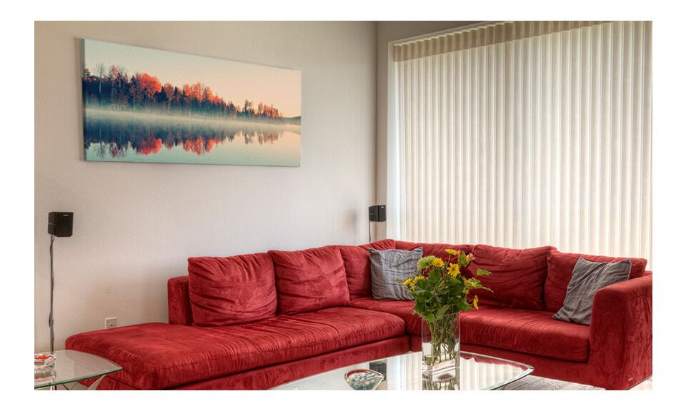 Wiszący na ścianie nad czerwoną kanapą obraz na płótnie przedstawiający drzewa nad jeziorem.