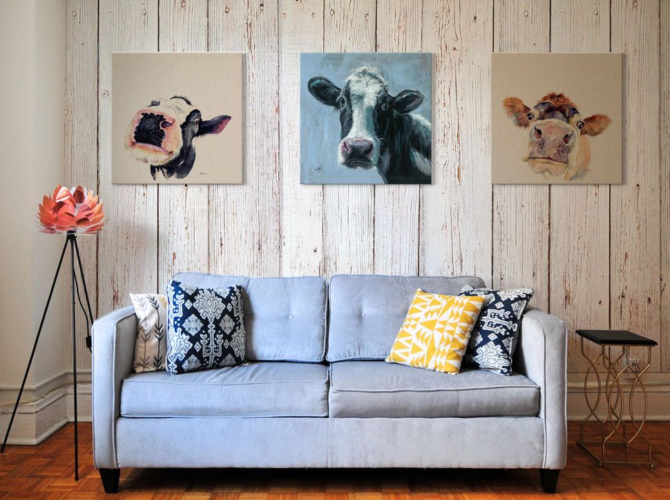 Obraz na płótnie z krową Judy wiszący na drewnianej ścianie w salonie nad błękitną kanapą