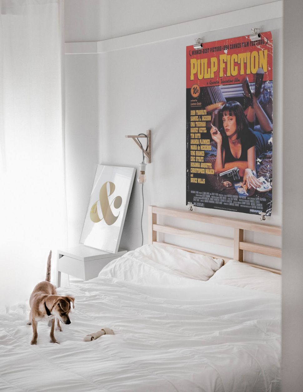 Plakat z filmu Pulp Fiction z Mią wiszący w sypialni nad drewnianym łóżkiem z białą pościelą
