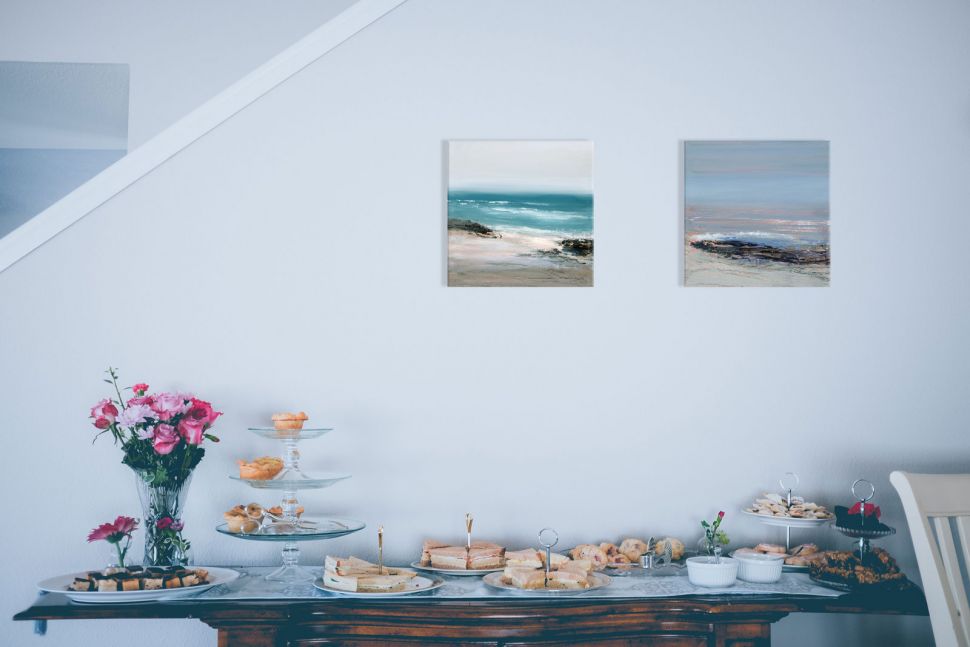 Canvas z krajobrazem morskim powieszony na białej ścianie nad stołem ze słodyczami