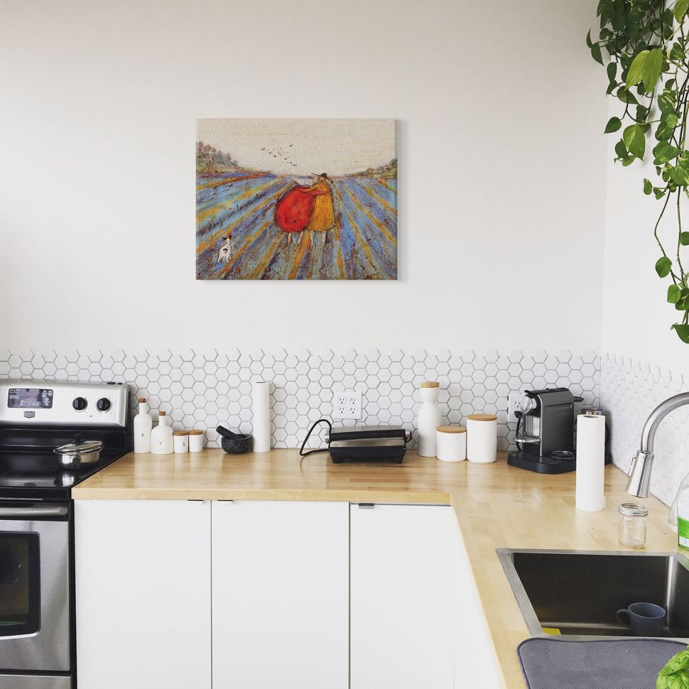 Obraz na płótnie autorstwa Sam Toft powieszony w kuchni nad biało drewnianymi szafkami