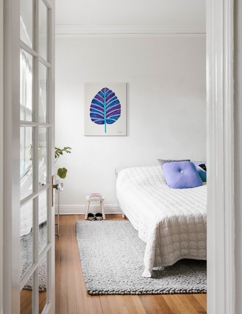 Canvas z liściem w kolorze indygo wiszący na białej ścianie nad łóżkiem w sypialni