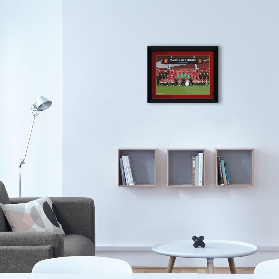 Obraz w czarnej ramce z klubem Manchester United powieszony w salonie nad półką