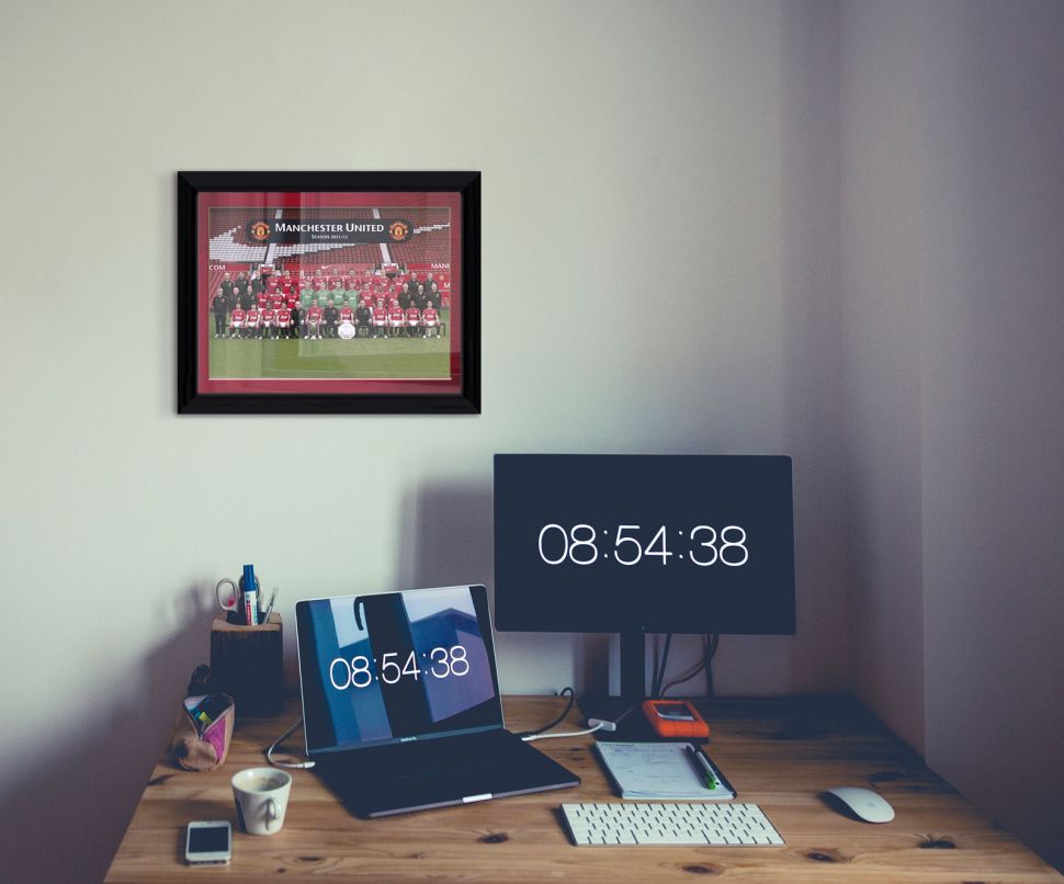 Obraz w czarnej ramce z zespołowym zdjęciem Manchesteru United powieszony nad drewnianym biurkiem