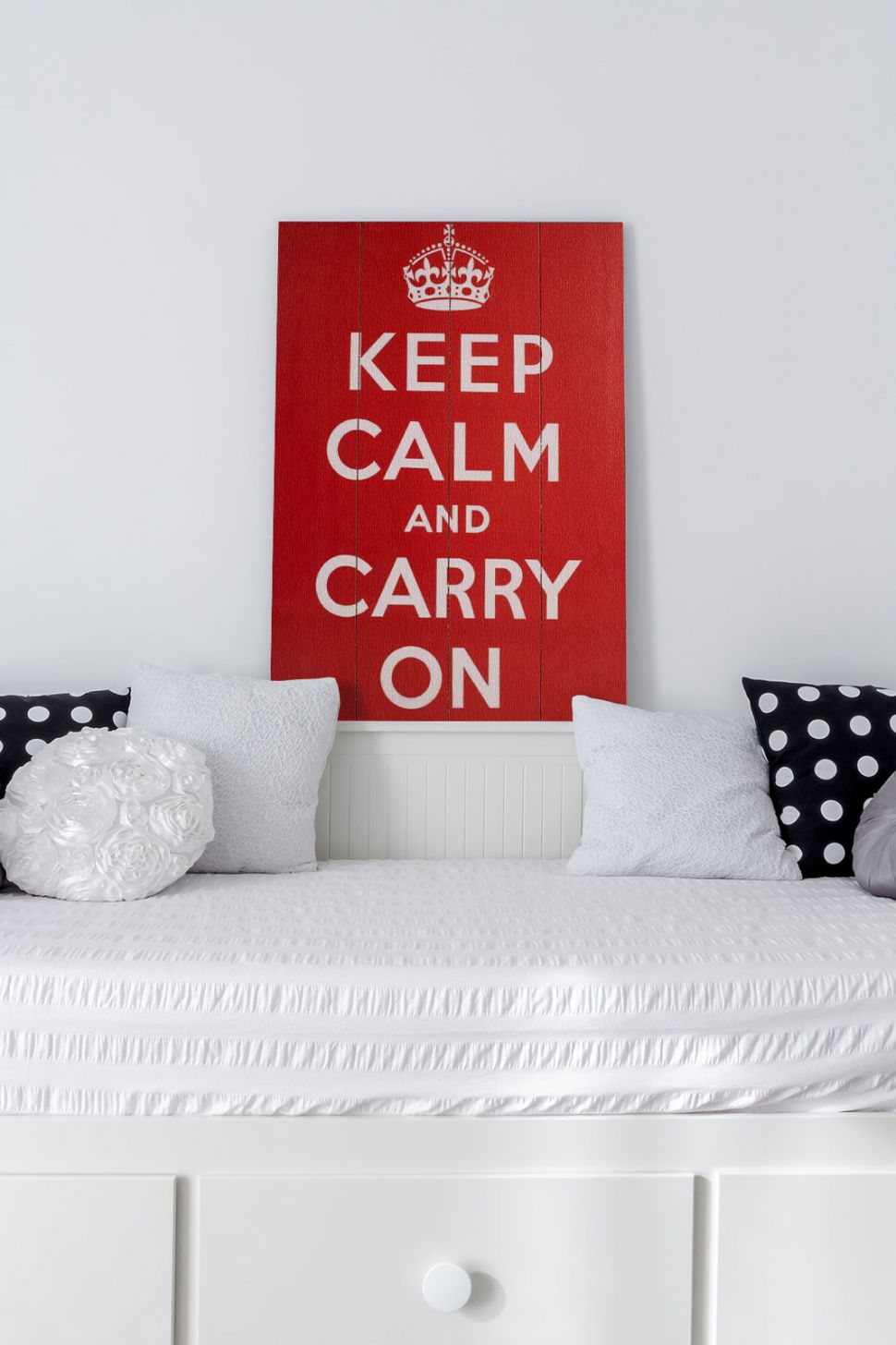 Obraz z napisami Keep Calm and Carry On wiszący na białej ścianie w pokoju