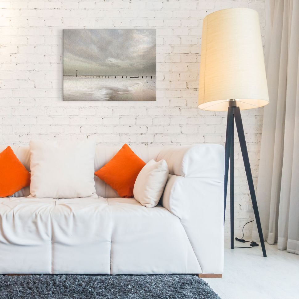 Obraz na płótnie przedstawiający morze i molo powieszony w salonie nad białą kanapą z pomarańczowymi poduszkami
