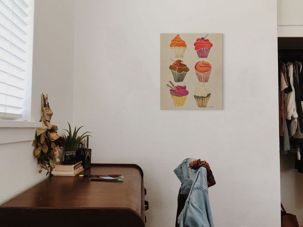 Obraz na płótnie wiszący na ścianie obok szafy z ubraniami przedstawiający kolorowe babeczki