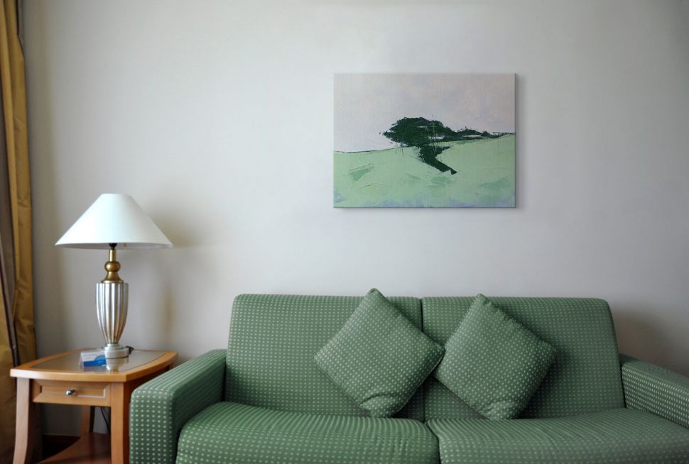 Canvas przedstawiający łąki z drzewami powieszony w salonie nad zielona kanapą