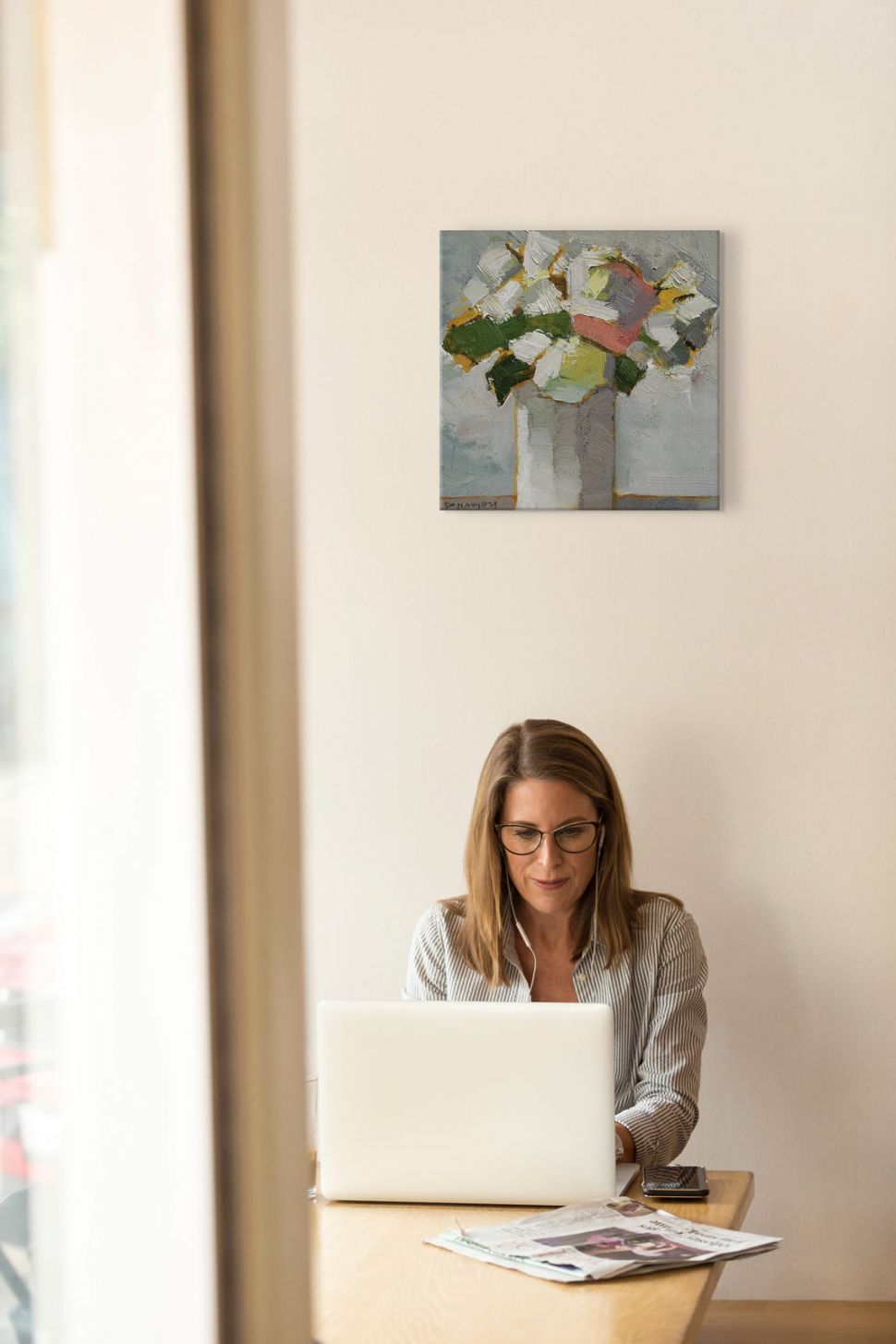 Obraz na płótnie wiszący w biurze na białej ścianie nad pracującą kobietą przedstawiający kwiaty we flakonie