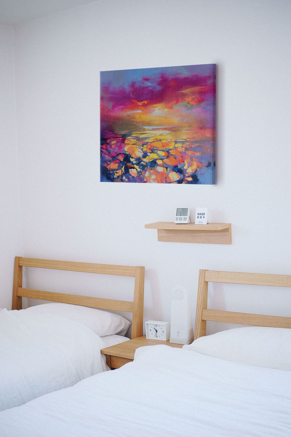Canvas z kolorową abstrakcją zatytułowany Red Hope powieszony nad dwoma drewnianymi łóżkami z białą pościelą