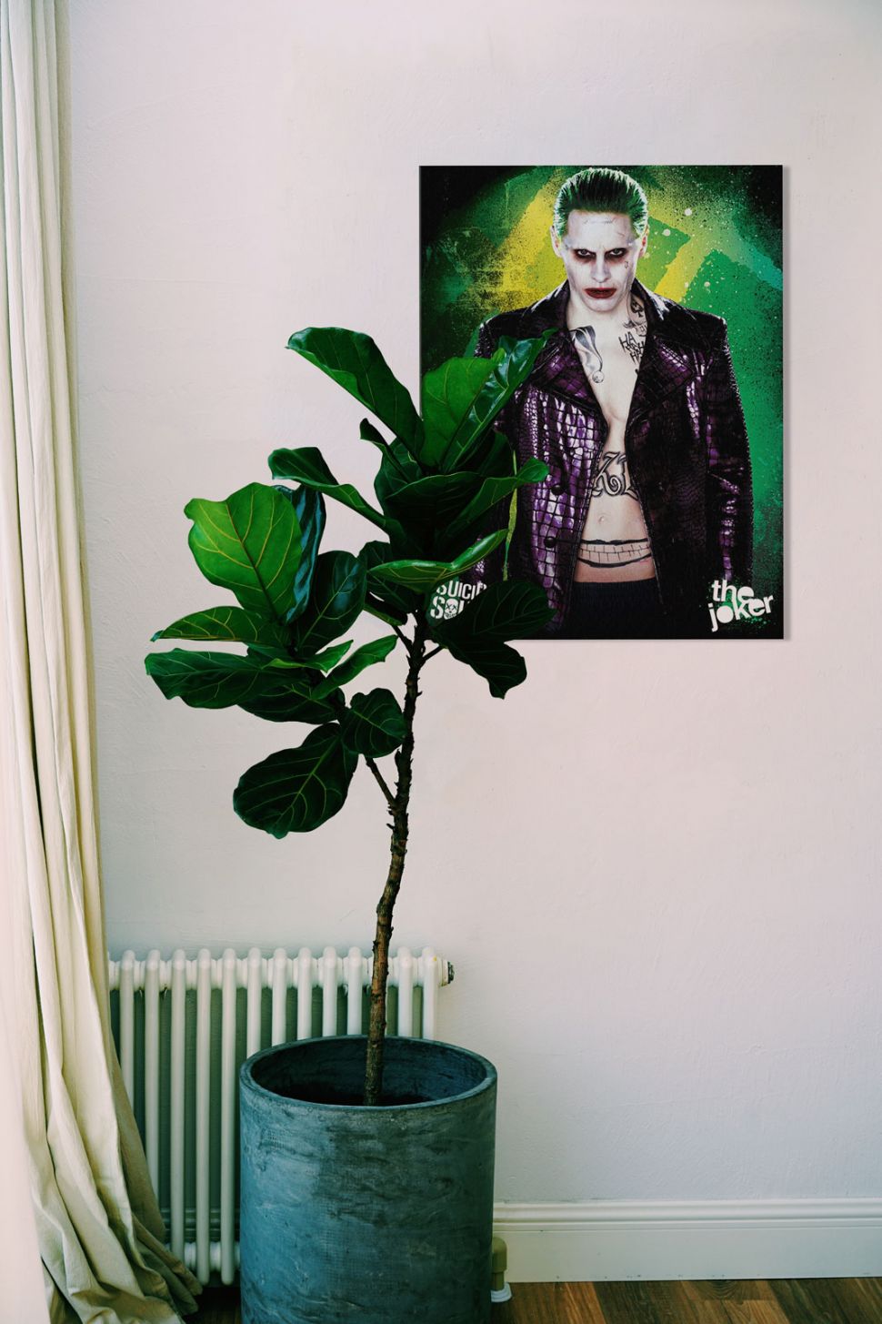 Obraz na płótnie przedstawiający Jokera z filmu Legion Samobójców wiszący na białej ścianie obok dużego kwiatka
